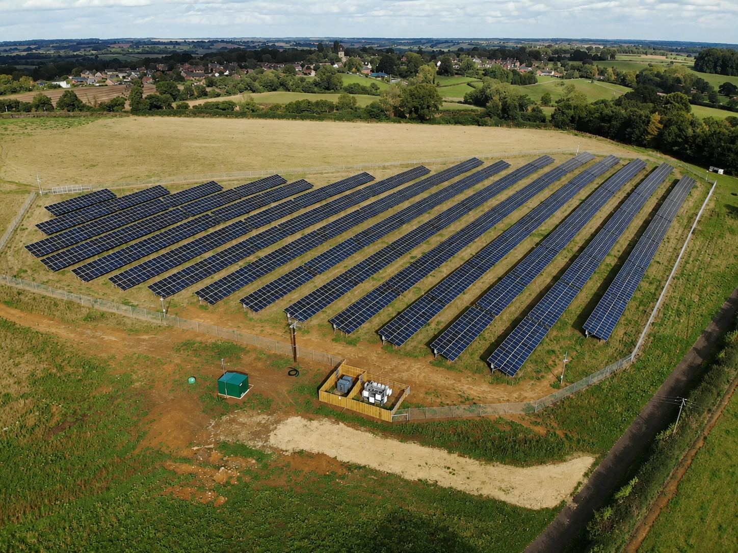 Aerial view of the completed 1.5MW solar array at Grovelands Business Park, East Haddon — rows of ground-mounted panels in a fenced field with the Northamptonshire countryside beyond